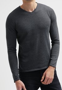 Camiseta de manga larga color gris oscuro con cuello en V, confeccionada en tela suave, con un diseño ajustado y detalles de costuras a lo largo del dobladillo y los puños.