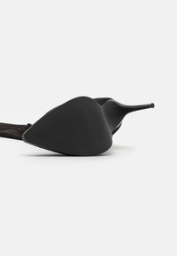 Zapato de tacón alto negro con punta afilada y suela negra texturizada, con un material superior suave y un diseño de tacón elegante.