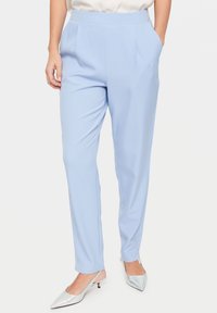 Světlomodré kalhoty na míru z hladké látky, s předními sklady a postranními kapsami, doplněné o stříbrné slingback lodičky.