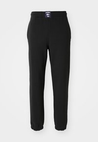Sorte joggebukser laget av mykt stoff, med elastisk linning, ribbestrikkede hem, og et Lacoste-logo-bånd bak.