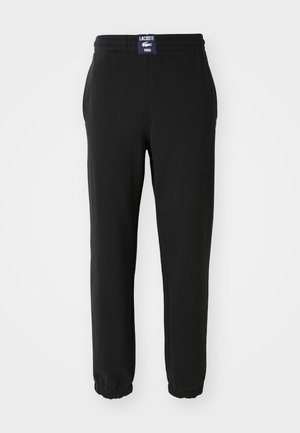 Black sweatpants made of soft fabric, featuring an elastic waistband, cuffed hems, and a Lacoste logo tag on the back.