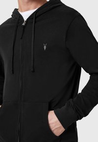 Felpa nera con zip realizzata in tessuto morbido. Presenta un emblematico teschio di capra in argento minimalista sul petto e tasche standard.