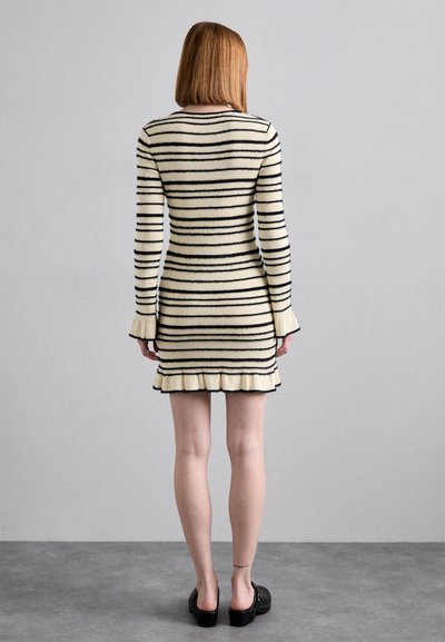 Knit dress with black stripes on a cream background, fitted design, fluted cuffs, and ruffled hem, paired with black footwear.