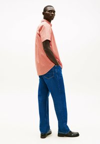 Camisa de rayas roja y blanca de manga corta, combinada con vaqueros azules y zapatos negros, con una silueta ajustada y un diseño casual.