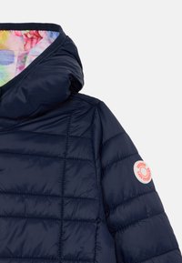 Navy insulated jacket with a quilted design, featuring a colorful floral interior lining and a circular logo patch on the sleeve.
