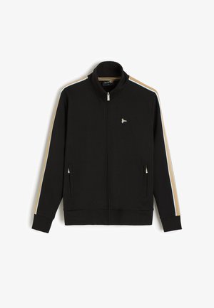 Czarna kurtka na zamek błyskawiczny z beżowymi i jasnoniebieskimi paskami na rękawach, kieszeniami na zamek po bokach, wysokim kołnierzem i małym białym logo na piersi.