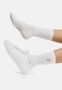 Calze bianche a coste con un design ricamato di cono gelato, abbinate a sneaker bianche con una finitura liscia e chiusura con lacci.