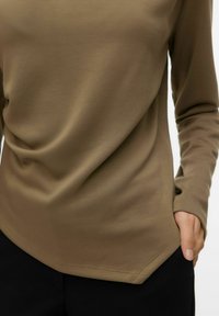 Olivengrønn langermet skjorte laget av glatt stoff, med rundet kant og en sidelomme, kombinert med svarte bukser.