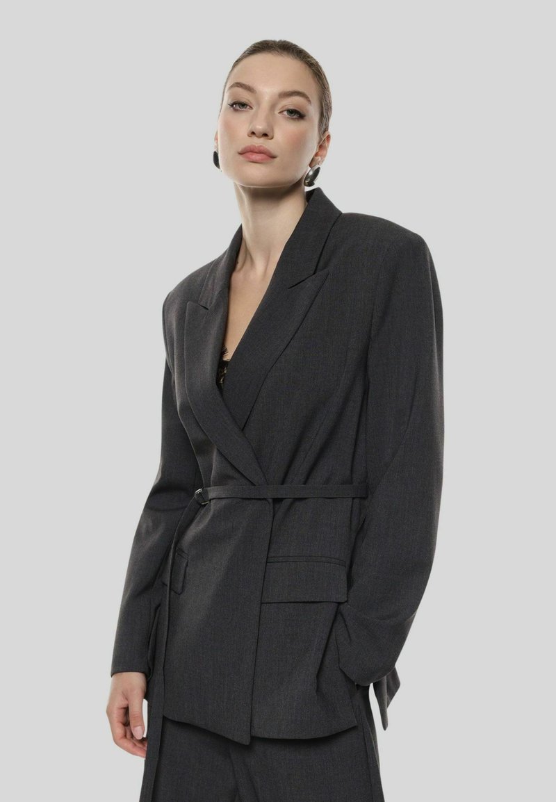 Blazer su misura grigio scuro con vita cinturata, rever affilati, chiusura a un bottone e tasche frontali, realizzato in tessuto testurizzato.