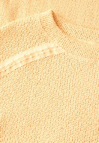 Ljust orange, strukturerad stickad tröja med rund halsringning och ett kontrasterande krämfärgat horisontellt band med upphöjda prickar över axlarna.