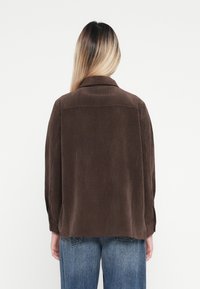 Braune Cordjacke mit einem Kragen, strukturierter Rippstruktur und langen Ärmeln, kombiniert mit hellblauen Jeans.