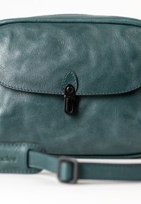 Borsa a tracolla in pelle teal con una texture liscia, una parte anteriore arrotondata e una chiusura a scatto in metallo nero. Dotata di una tracolla regolabile.