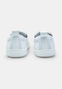 Adidași albi cu un superior din piele netedă și suede, formă rotundă, două manere în spate și o talpă din cauciuc texturat.