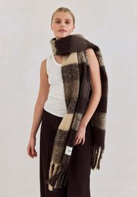 Geruite wollen sjaal in bruin- en crèmetinten, met franjes aan de uiteinden. Zachte textuur en warm ontwerp. Label zichtbaar op de sjaal.