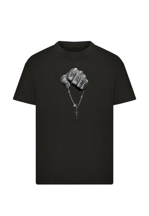 T-shirt noir avec un graphisme d'un poing tenant un chapelet, doigts tatoués avec le mot "PRAY," et un pendentif croix brillant.