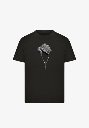 T-shirt noir avec un graphisme d'un poing tenant un chapelet, doigts tatoués avec le mot "PRAY," et un pendentif croix brillant.