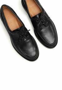 Černé kožené boty s hladkým povrchem, kulatou špičkou a kontrastními tkaničkami. Minimalistický design, který zahrnuje šitý podrážku a značení na stélce.