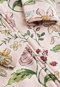 Stoff mit floralen Mustern in sanftem Pink, der eine Mischung aus Gelb, Rot und Grün zeigt. Bemerkenswerte Details sind die umgeschlagenen Ärmel und die feine Naht.