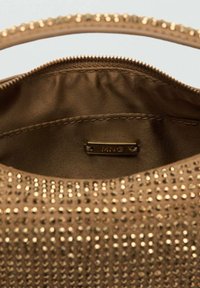 Intérieur d'un sac à main brun avec une texture lisse, comportant des rivets métalliques et une petite étiquette en métal portant la mention "MNG". Matériau doux et doublé.