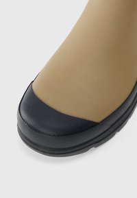 Bruine rubberen laars met een getextureerde zwarte neuskap en een gladde beige schacht, met een ronde vorm en een duurzame zool.