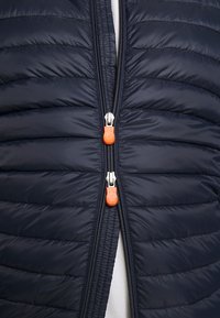 Marineblå dynejakke med vandrette syninger, udstyret med dobbelte lynlåse og orange trækflipper. Glat, skinnende stof med et letvægtsdesign.