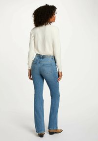 Jeans a zampa d'elefante di un blu chiaro con una cintura intrecciata testurizzata. Quattro tasche e dettagli di cucitura visibili sul retro. Finitura del tessuto liscia.