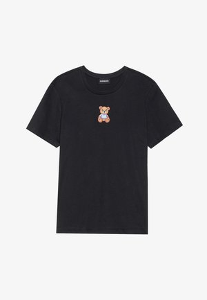 Camiseta de algodón negra con un pequeño oso de peluche bordado en un traje azul en el pecho. Cuello redondo y mangas cortas.
