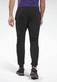 Black sweatpants with a tapered design, elastic cuffs, and side pockets, paired with black sneakers. Smooth, lightweight fabric.