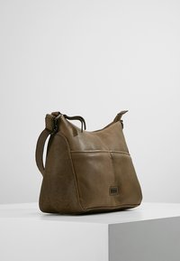 Ruskea nahkainen olkalaukku säätövarsilla, suorakulmainen etutasku ja huomaamaton brändilogo etupaneelissa, asetettuna valkoiselle pinnalle.