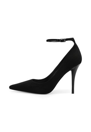 Scarpa nera con tacco alto, punta appuntita e sottile cinturino alla caviglia con fibbia su sfondo bianco.
