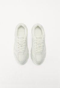 Zapatillas blancas con material de malla y sintético, de forma redondeada, con diseño de cordones y con una sutil marca en la plantilla.