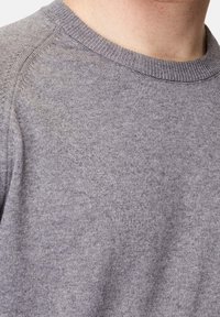 Grau gestrickter Pullover mit einem gerippten runden Halsausschnitt und glatter Textur. Der Stoff wirkt weich mit einem dezenten Strickmuster. Nahaufnahme.