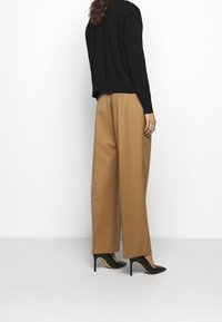 Czarny dziany sweter zestawiony z beżowymi spodniami o szerokich nogawkach oraz czarnymi butami na wysokim obcasie. Strój prezentuje luźny fason i miękkie tekstury.