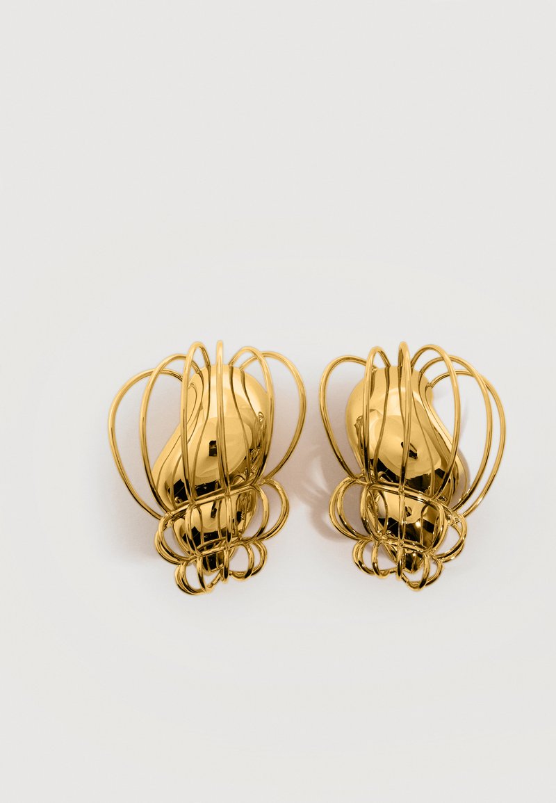 Ζευγάρι αφηρημένων σκουλαρικιών σε χρυσό τόνο με λείες κεντρικές φιγούρες περιβαλλόμενες από πολλούς καμπυλωτούς βρόχους από σύρμα, επάνω σε λευκό φόντο.