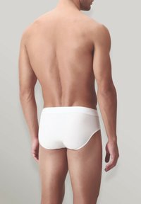 Slip in cotone bianco con una morbida fascia in vita, caratterizzati da una vestibilità aderente e una texture liscia, visti di schiena su uno sfondo neutro.