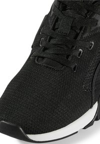 Chaussure de sport noire avec tige en tissu texturé, lacets noirs et semelle intermédiaire blanche, présentée en gros plan mettant l'accent sur la zone des orteils et des lacets.