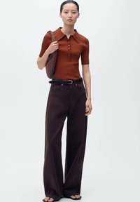 Polo shirt marron côtelé à manches courtes, patte de boutonnage ; pantalon large marron foncé taille haute ; sac à épaule ; sandales.