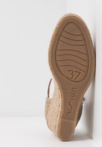 Semelle d'une chaussure tissée beige tenue verticalement, montrant la semelle en caoutchouc taille 37 et la marque Unisa.