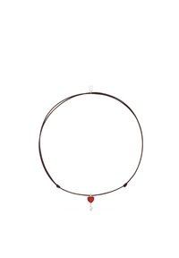 Collar de cordón marrón con un pequeño colgante de llave plateada con un lazo en forma de corazón rojo en el centro.
