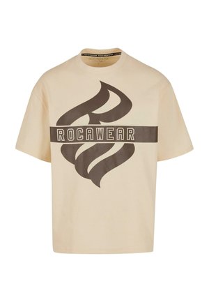 Beige cotton t-shirt with a large brown graphic design and "ROCAWEAR" text across the front. Features a crew neck and short sleeves.