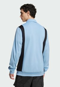 Chaqueta de pullover azul claro con paneles laterales negros, tejido texturizado, diseño con collar y mangas largas. Puños y bajo elásticos.