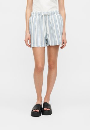 Vrouw draagt blauw-witte verticaal gestreepte short met trekkoord en zwarte platformsandalen, staand tegen een witte achtergrond.
