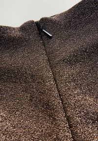 Gros plan d'un tissu marron métallique avec une fermeture éclair noire partiellement ouverte en haut au centre.