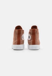 Zapatillas altas de lona naranja con suelas de goma blancas, que presentan logotipos redondos icónicos en los lados exteriores y un acabado texturizado.