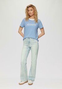 Lichtblauw gestreept t-shirt met de tekst "dream" in het wit, gecombineerd met licht denim flared jeans en witte sneakers met tan kleurige zolen.