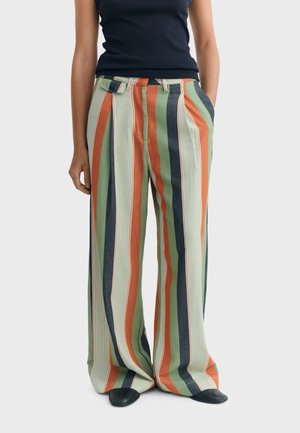 Person wearing high-waisted, wide-leg pants with vertical stripes in green, orange, cream, and black, paired with black shoes and a black top.