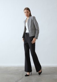Blazer grigio cropped in tessuto strutturato, con vestibilità su misura e colletto a scollo a V. Abbinato a pantaloni neri a zampa d'elefante e tacchi neri.