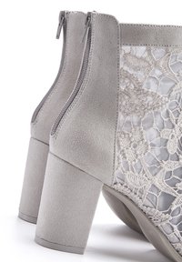 Graue Wildleder-Stiefeletten mit Schnürdetails, ausgestattet mit einem Blockabsatz und seitlichen Reißverschlüssen für ein einfaches An- und Ausziehen. Strukturierter Stoff hebt sich von glatten Akzenten ab.