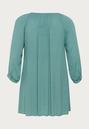 Blusa turchese con maniche a tre quarti, schiena plissettata e scollatura rotonda. Realizzata in tessuto leggero con una texture liscia.