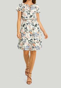 Robe courte à manches courtes en tissu léger avec une taille élastique. Elle présente un col rond et une jupe à volants. Accentuée par des motifs floraux colorés.